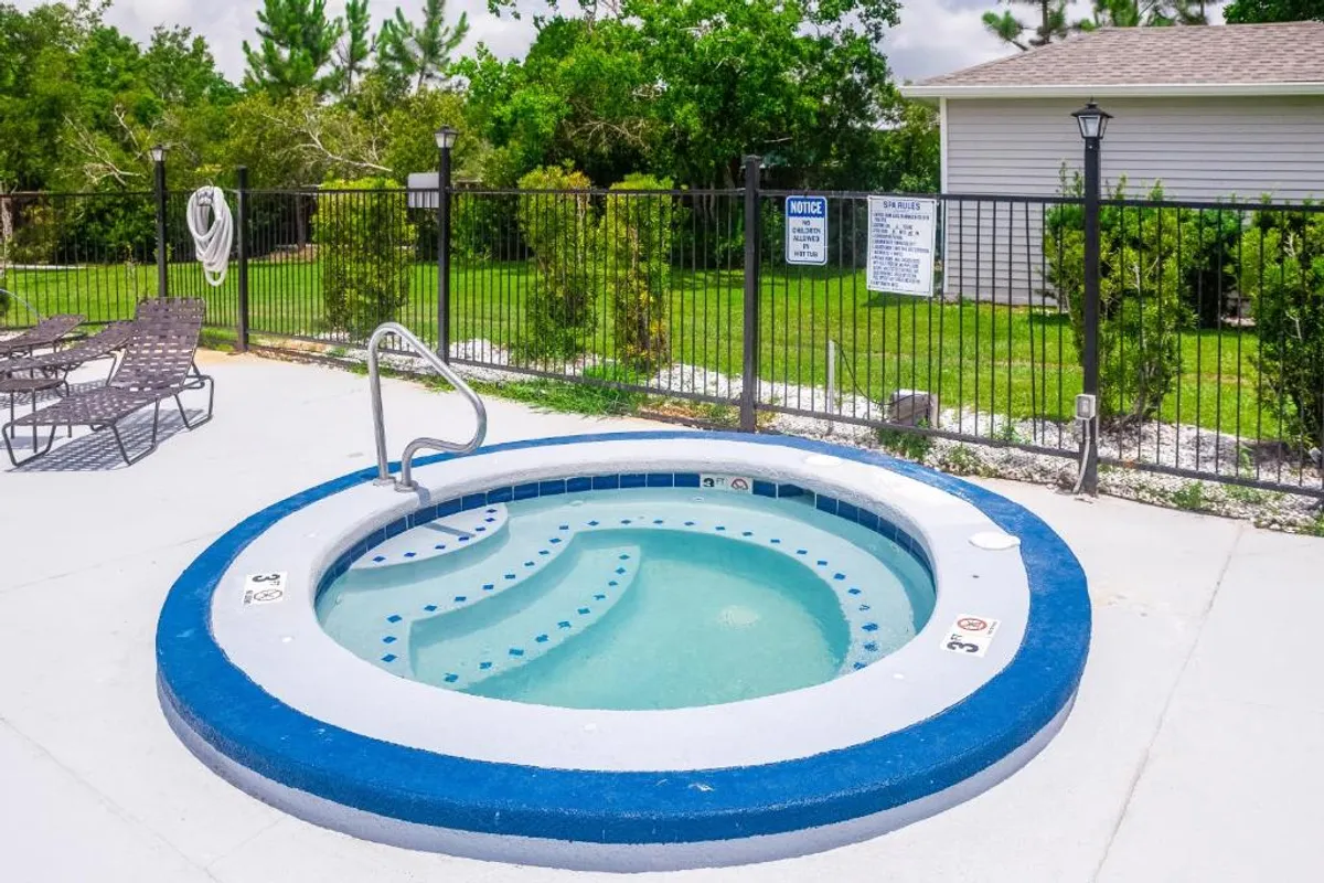 An exterior view of a tranquil hot tub area, nestled amidst lush greenery and furnished with comfortable lounge chairs. The inviting hot tub is the focal point, suggesting relaxation and opportunities to unwind or socialize, especially during cooler winter evenings. The mood is calm and inviting, with hints of sunset lighting.