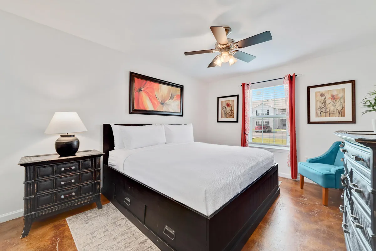 This image features a king bed with a neatly arranged nightstand, a window allowing in natural light, a chair, and wall art, all creating an inviting and tranquil bedroom atmosphere. The scene suggests comfort and a peaceful retreat—ideal for parents or couples.