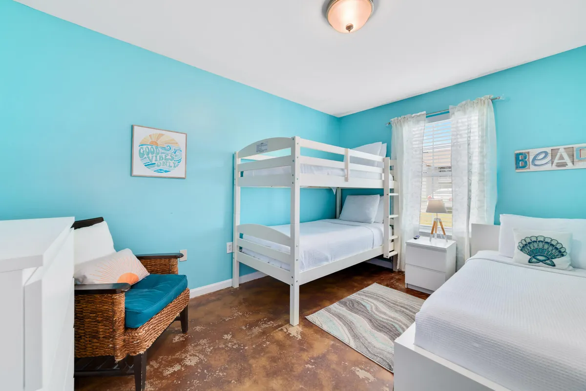 A playful kids' room with a twin bed and a twin-over-twin bunk bed, colorful wall art, and a woven chair. The arrangement is clearly designed for flexibility, sleepovers, and creative moments, perfect for children or extra guests.
