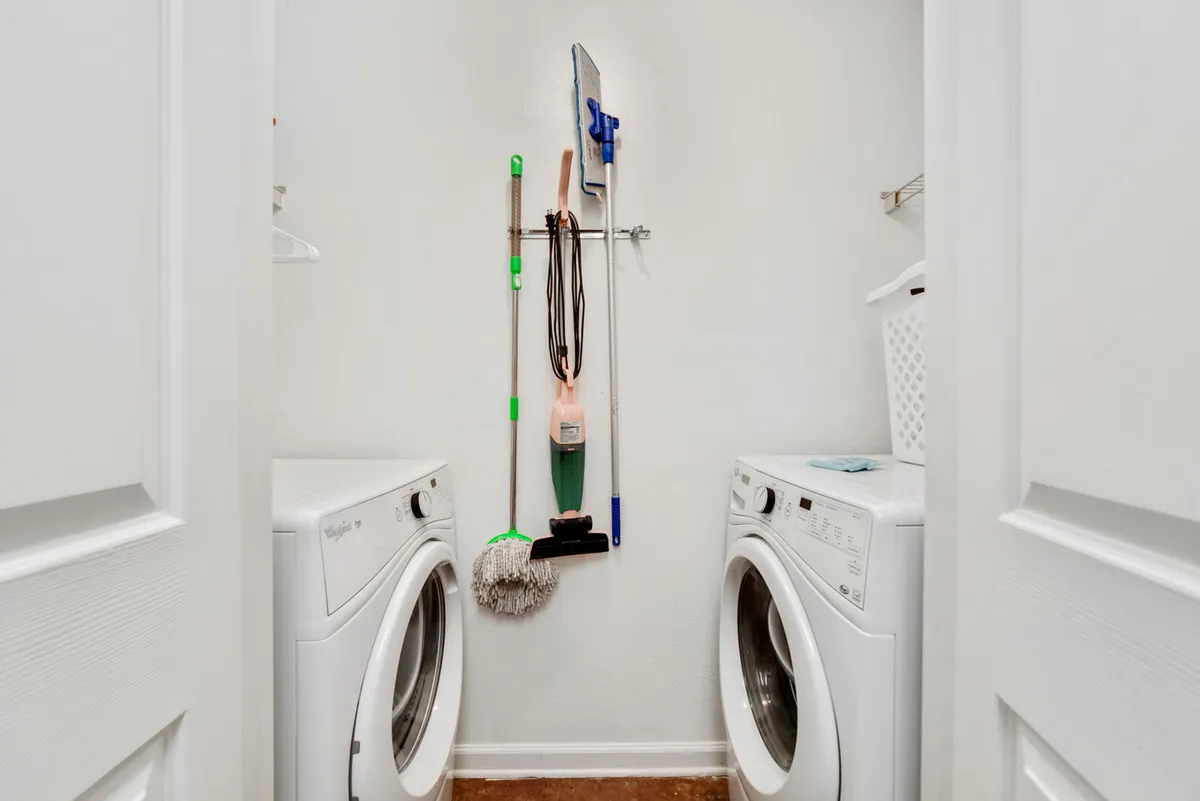 A practical laundry area with a full-size washer and dryer, cleaning supplies, and a laundry basket, all neatly organized. The setup conveys convenience and the ability to stay fresh during extended stays.